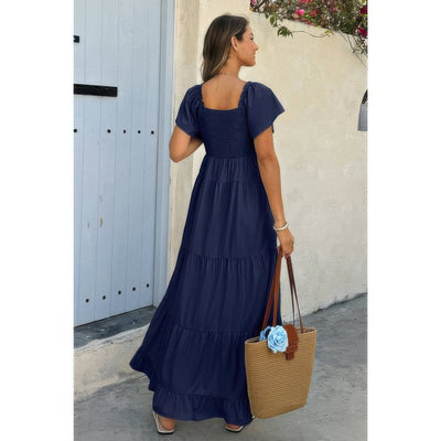 Woman wearing navy square neck ruffle hem dress with smocked bodice and puff sleeves holding straw tote