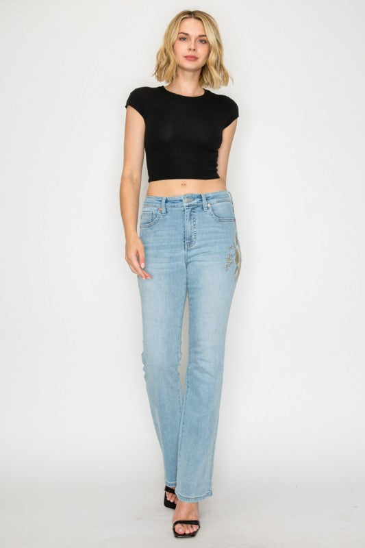 Artemis Vintage model wearing women's high rise embroidered bootcut jeans in light wash with floral side embroidery