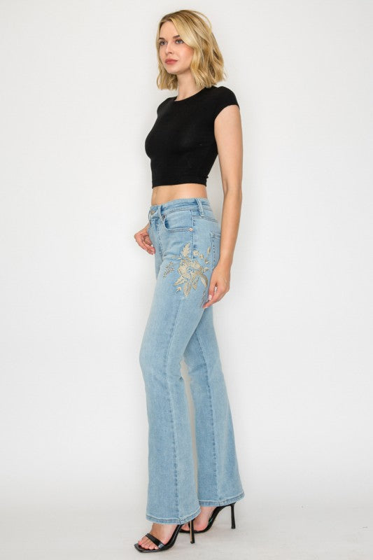 Artemis Vintage model wearing women's high rise embroidered bootcut jeans in light wash with floral embroidery and black crop top