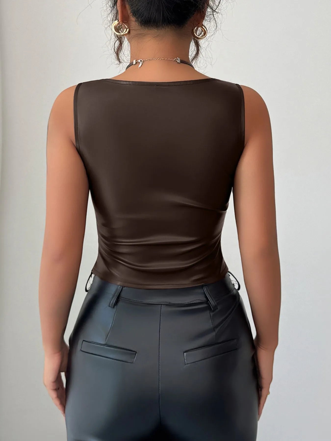 Back view of model wearing Trendsi women's faux leather tank top in chocolate brown paired with black faux leather pants