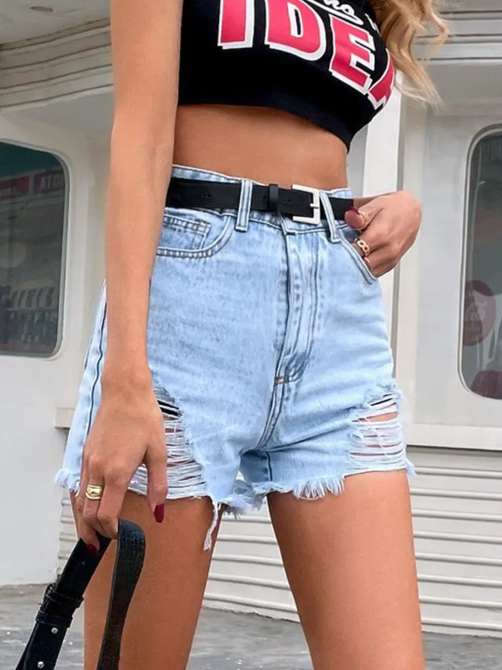 Trendsi model wearing light wash high waist distressed denim shorts for women with black belt and crop top