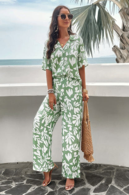 Woman wearing green floral print front button blouse set with wide leg pants straw tote and sunglasses at beach