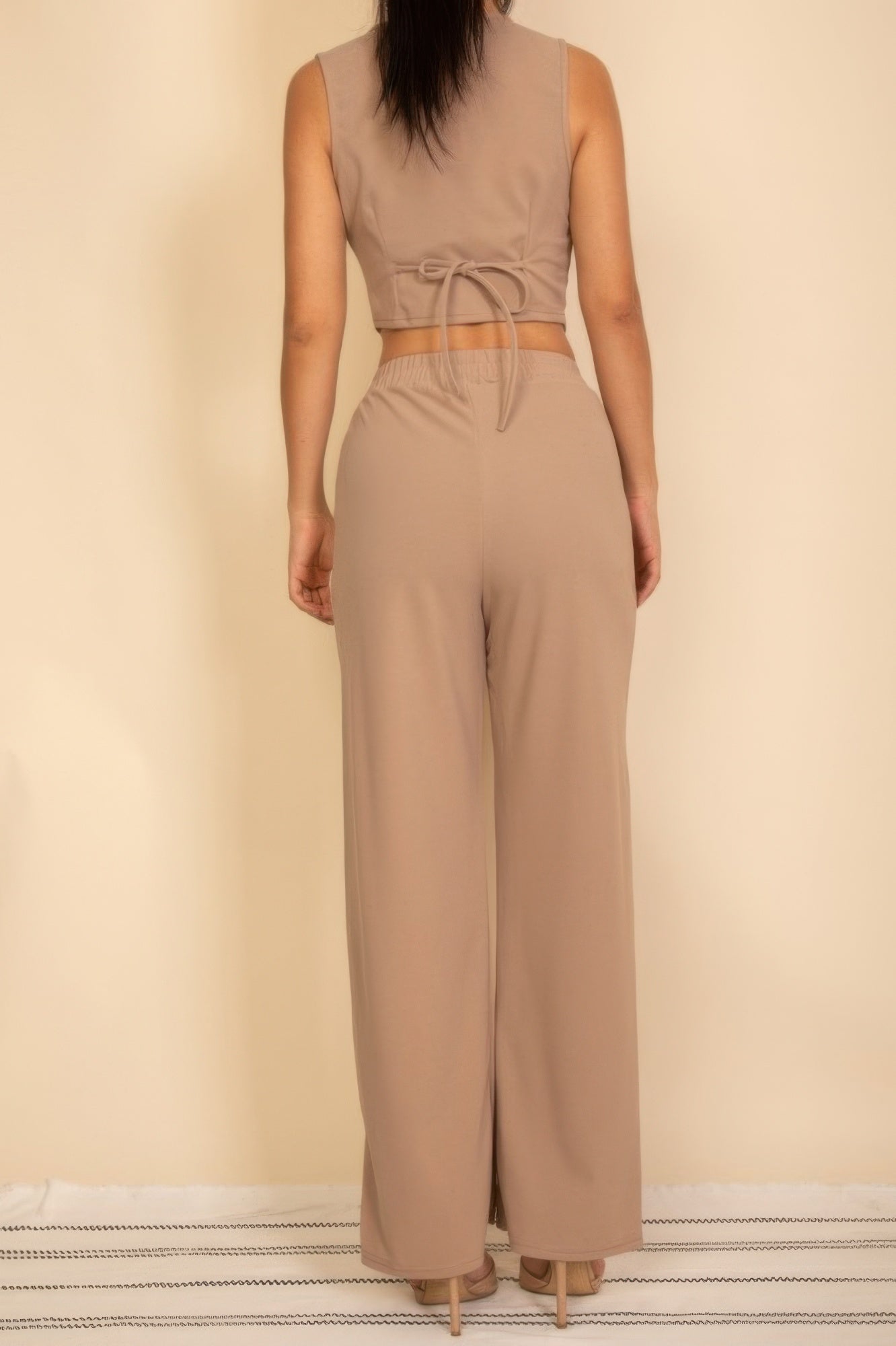 Back view of a woman wearing a tailored button vest in beige with matching wide-leg pants