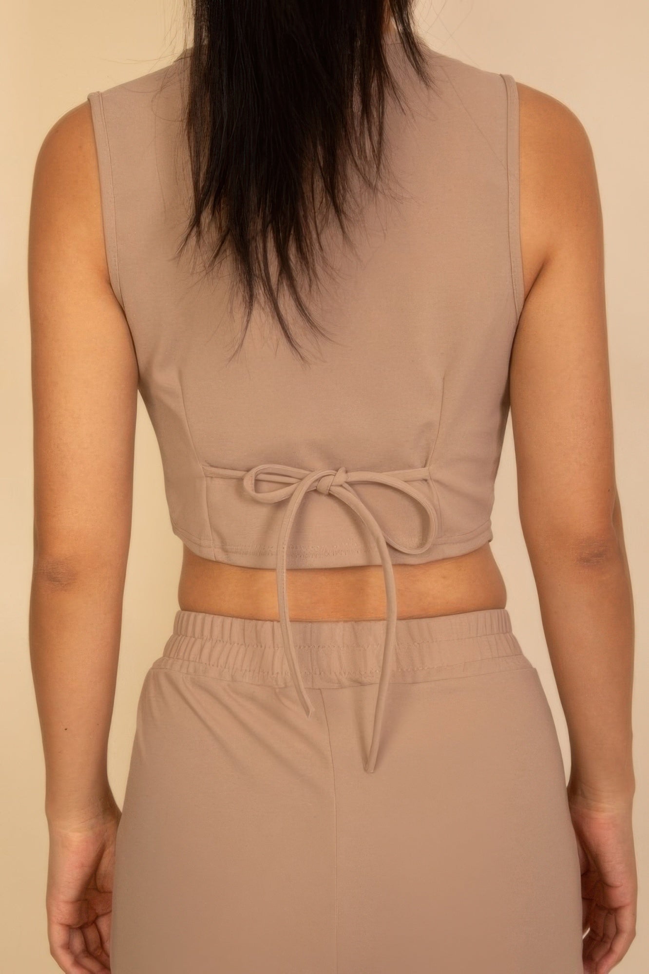 Back view of a tailored button vest in beige with a tie closure for a stylish fit