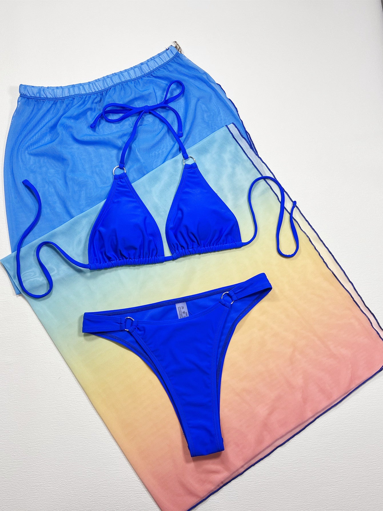 Trendsi three piece bikini set with skirt in vibrant blue laid flat on gradient beach towel
