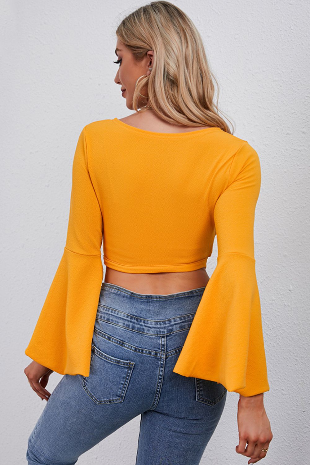Back view of a yellow Tie Front Cropped Top with bell sleeves paired with denim jeans