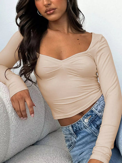 Chic woman wearing a Trendy Fitted Tee in beige with long sleeves, styled with high-waisted jeans.