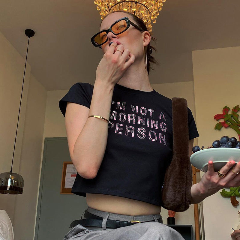 Trendsi model wearing black Crop T-Shirt that reads Im Not a Morning Person with sunglasses gray pants and a bowl of fruit