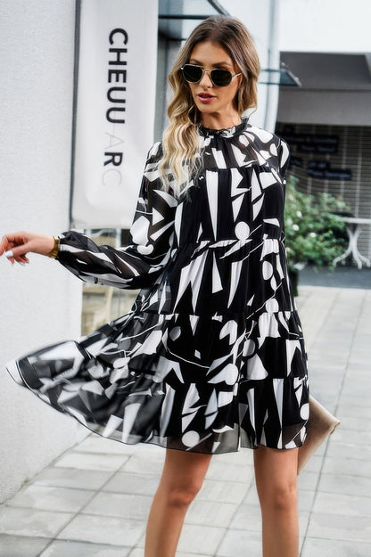 Woman wearing black and white abstract print tiered dress with long sleeves and sunglasses walking outdoors